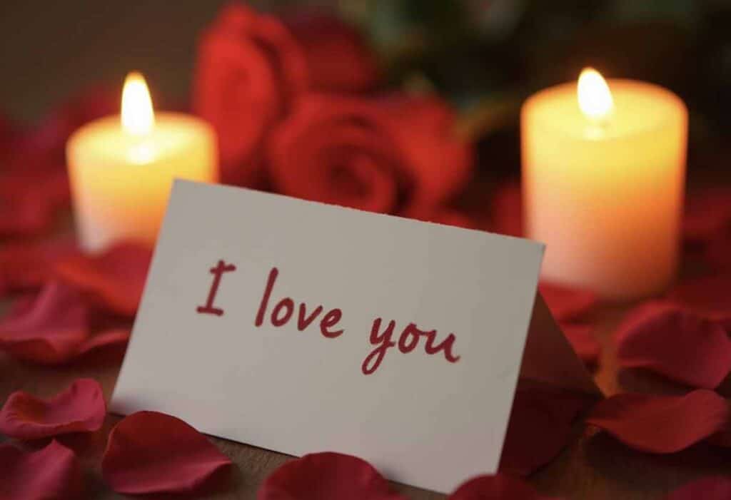 A handwritten note saying "I love you" surrounded by candlelight and rose petals, creating a romantic and tender atmosphere.