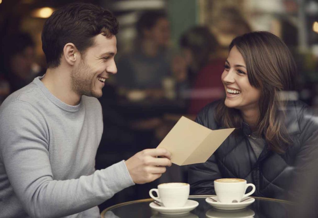 Friends laughing over coffee, one holding a handwritten card.