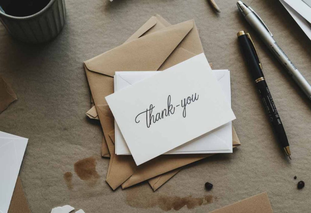 Flat-lay of thank-you cards and envelopes with pens and coffee stains.